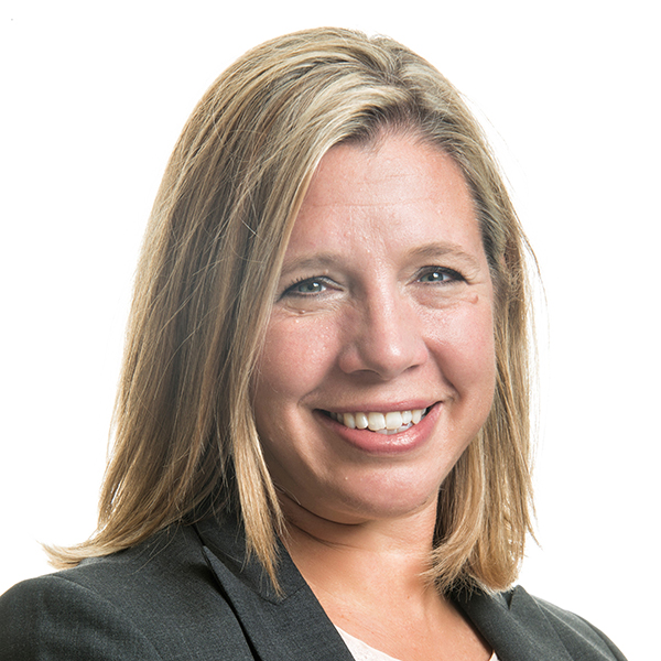Woman with straight blonde hair wearing a dark blazer, smiling at the camera against a plain white background.